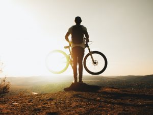 Homme devant un coucher de soleil en montagne, portant son vélo