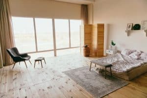 Chambre avec un grand tapis au bout du lit, une baie vitrée et un fauteuil