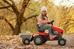 Petite fille faisant du tracteur à pédales sur un chemin en forêt