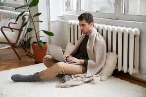 homme assis entouré d'une couverture et collé au chauffage